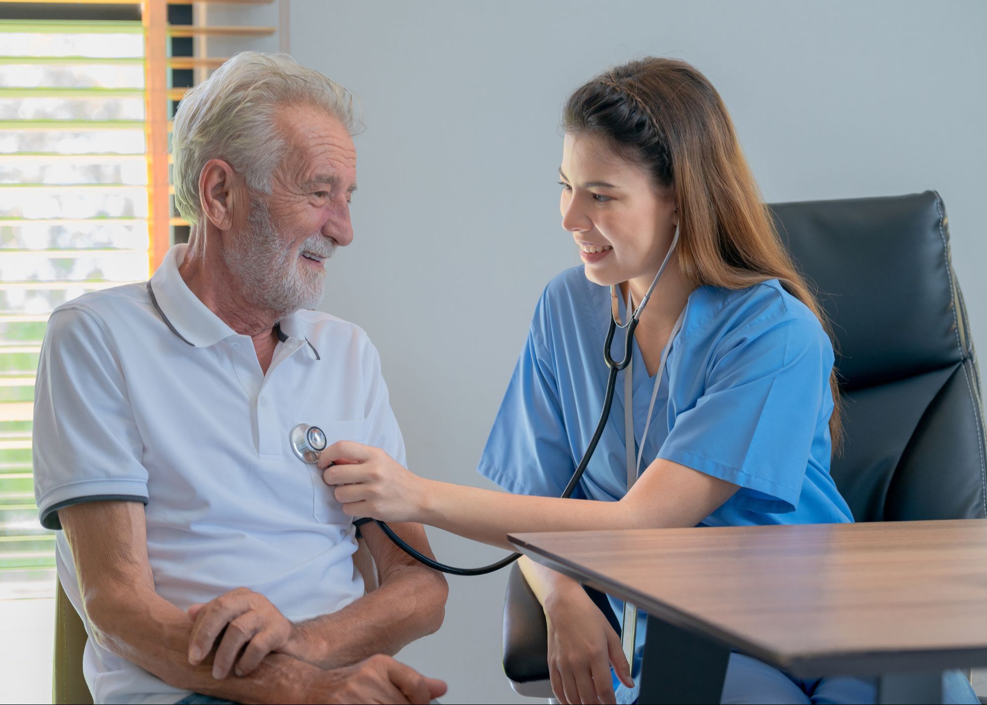 Healthcare professional using a stethoscope on a smiling elderly male patient during a medical check-up.