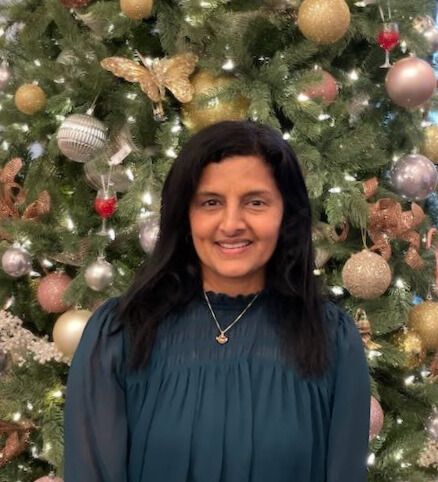 Dr. Yadalla with a joyful expression, standing in front of a festive Christmas tree adorned with sparkling ornaments.