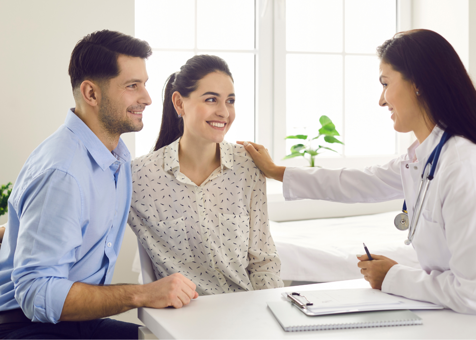 A doctor reassuring a smiling woman with a supportive male companion by her side during a consultation in a bright medical office