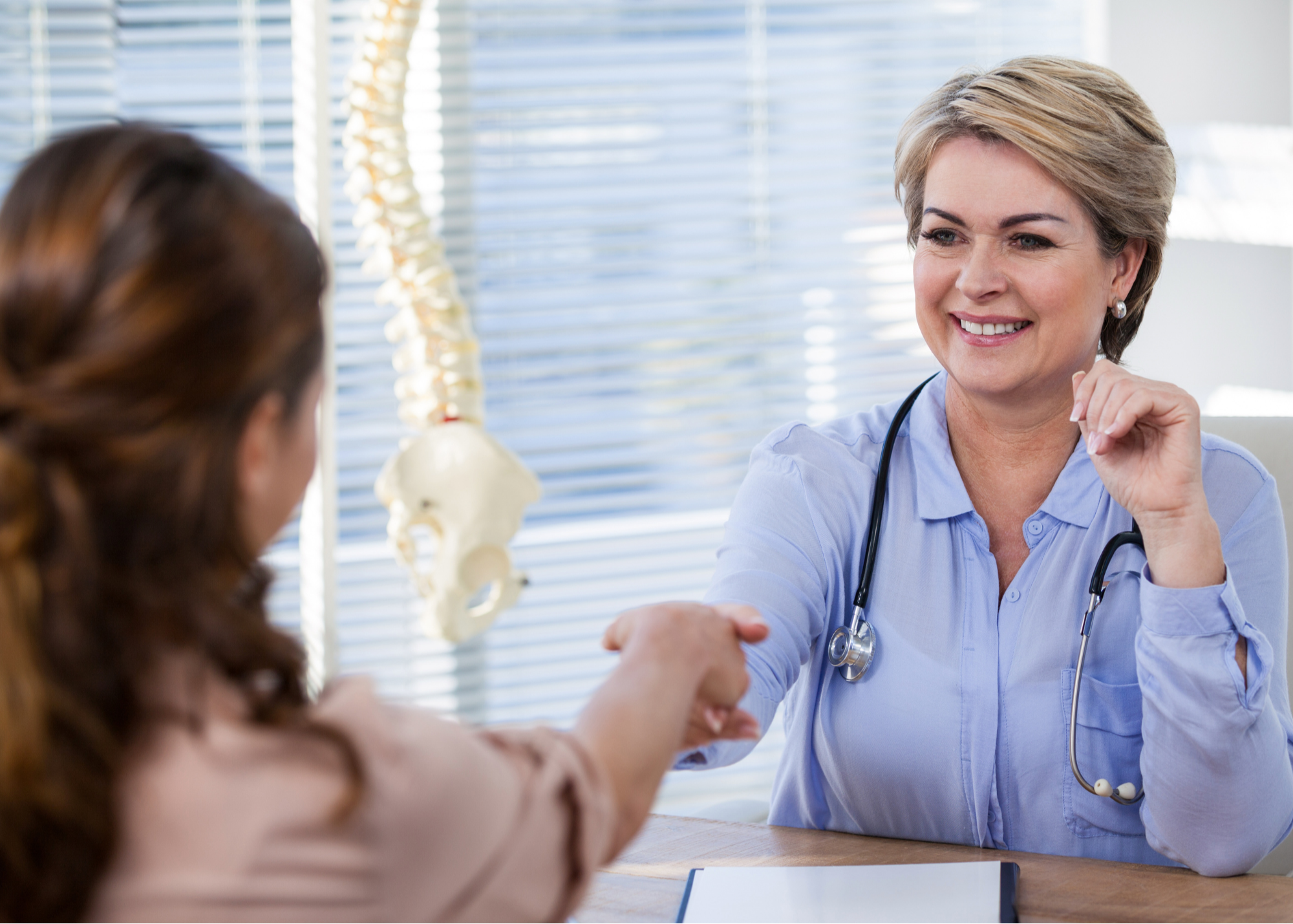 A smiling physician shaking hands with a patient across a desk