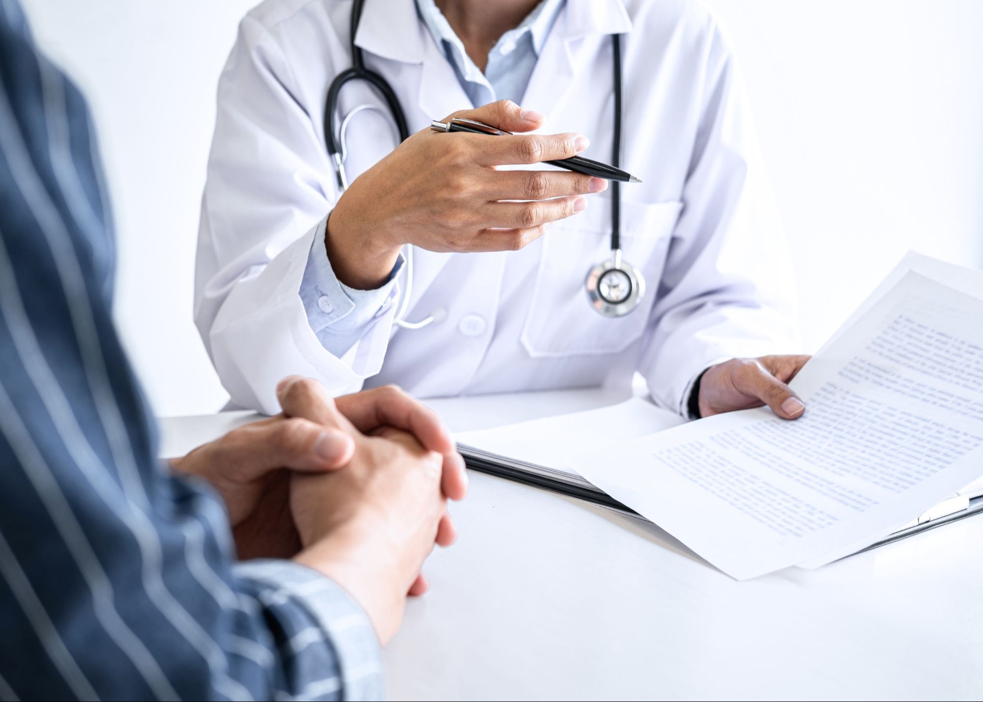 Close-up of a doctor's hands holding a pen, discussing a treatment plan with a patient, with a stethoscope visible, symbolizing professional medical consultation.