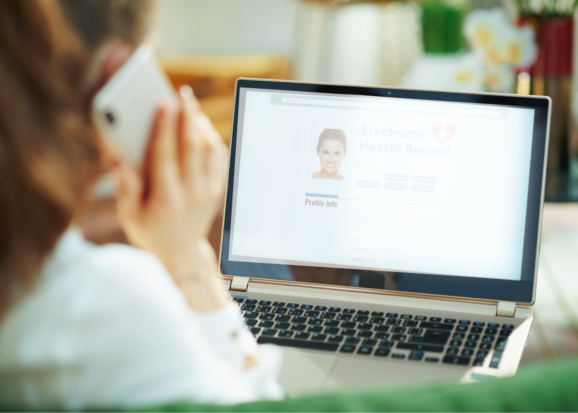 A physician is seen from behind viewing an electronic health record on a laptop screen while having a phone conversation, indicating a medical professional engaging in patient care.